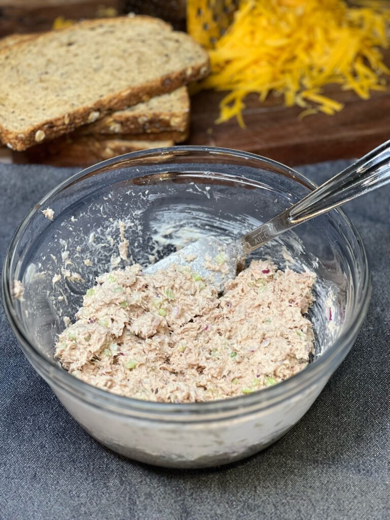 Tuna mixed with mayo, celery and red onion to make tuna salad in a clear glass bowl.