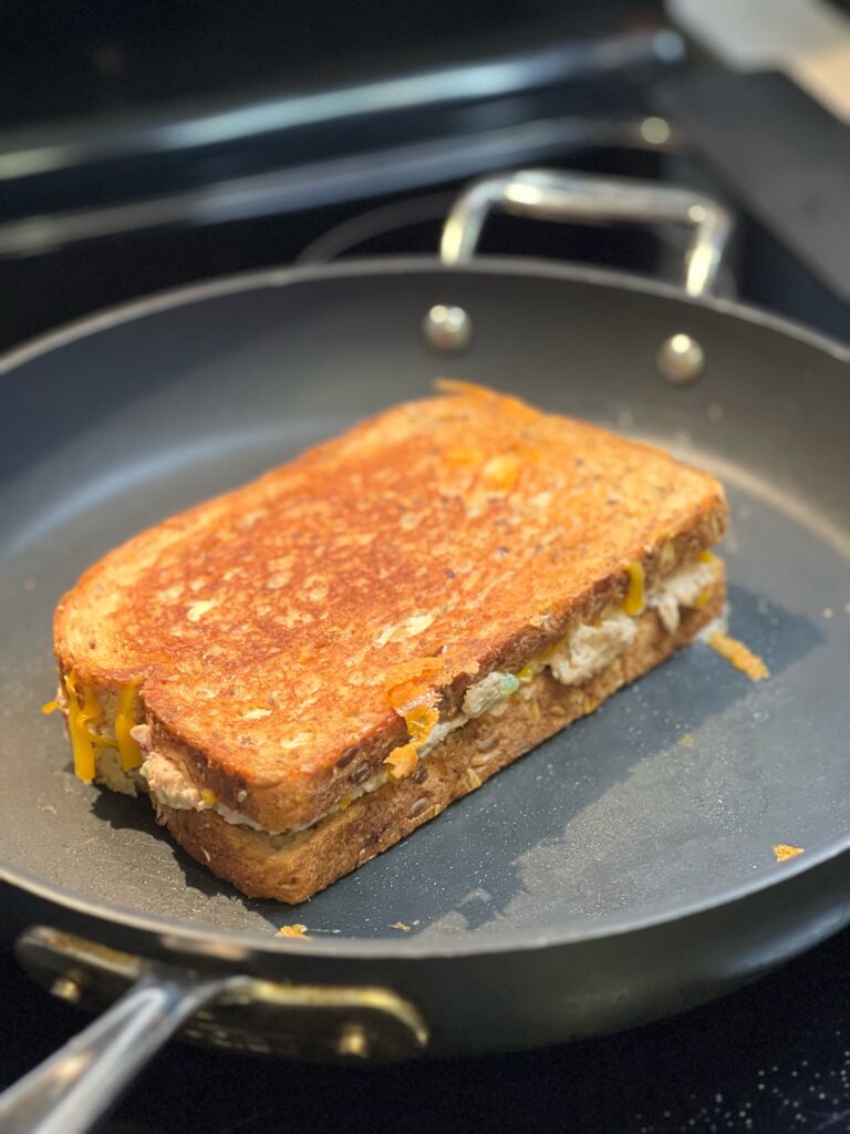 A tuna melt on grainy bread toasting in a non-stick pan.