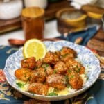 A bowl of steamed rice topped with crispy salmon bites that are drizzled with a honey lemon cream sauce and garnished with fresh parsley.