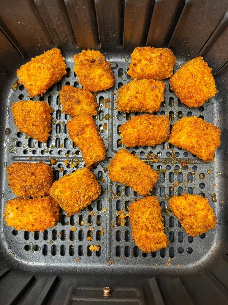 Crunch salmon bites in an air fryer basket. The salmon bites are golden brown on the outside.