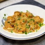 A white plate of seared scallops covered in miso cream sauce and garnished with microgreens and sesame seeds.