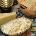 A tan, boat-shaped bowl filled with Jarlsberg Cheese Dip. The shredded cheese is mixed with a mayo-based sauce. The dip is garnished with cracked black pepper.