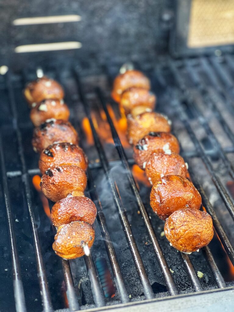 Two metal skewers holding brown mushrooms placed on the grill.