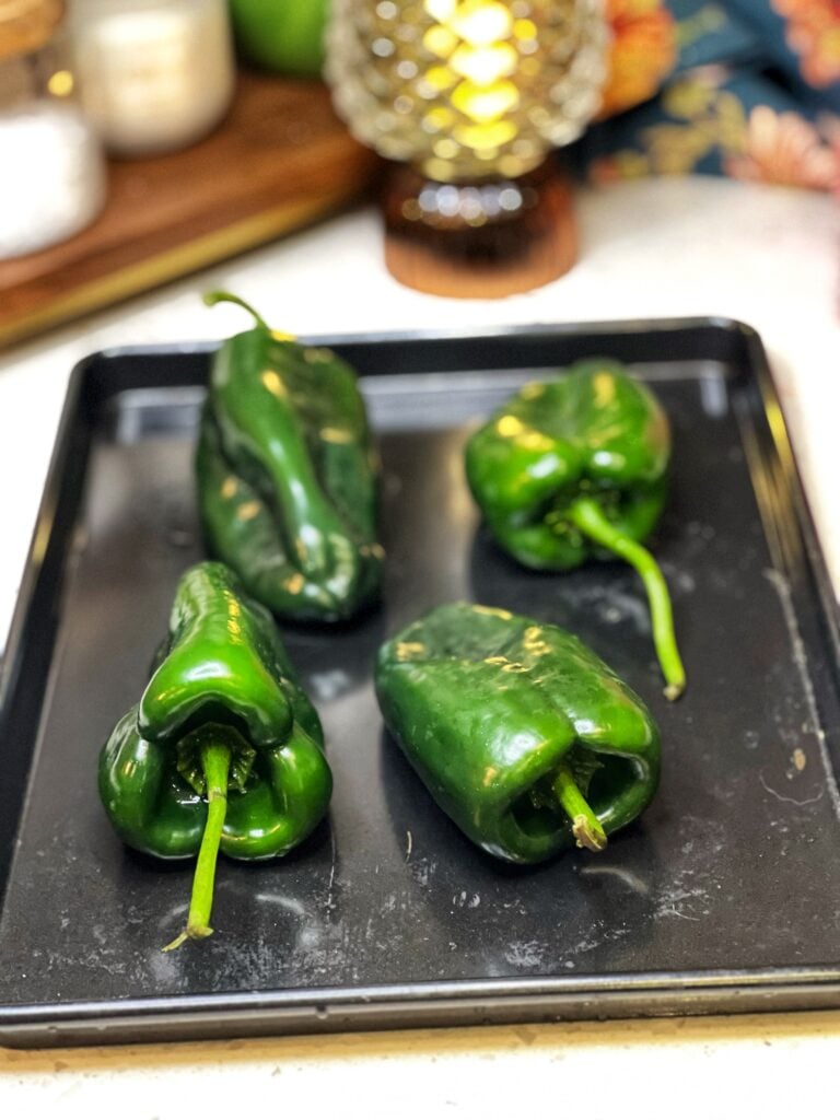 Four poblano peppers laying on a black baking sheet.
