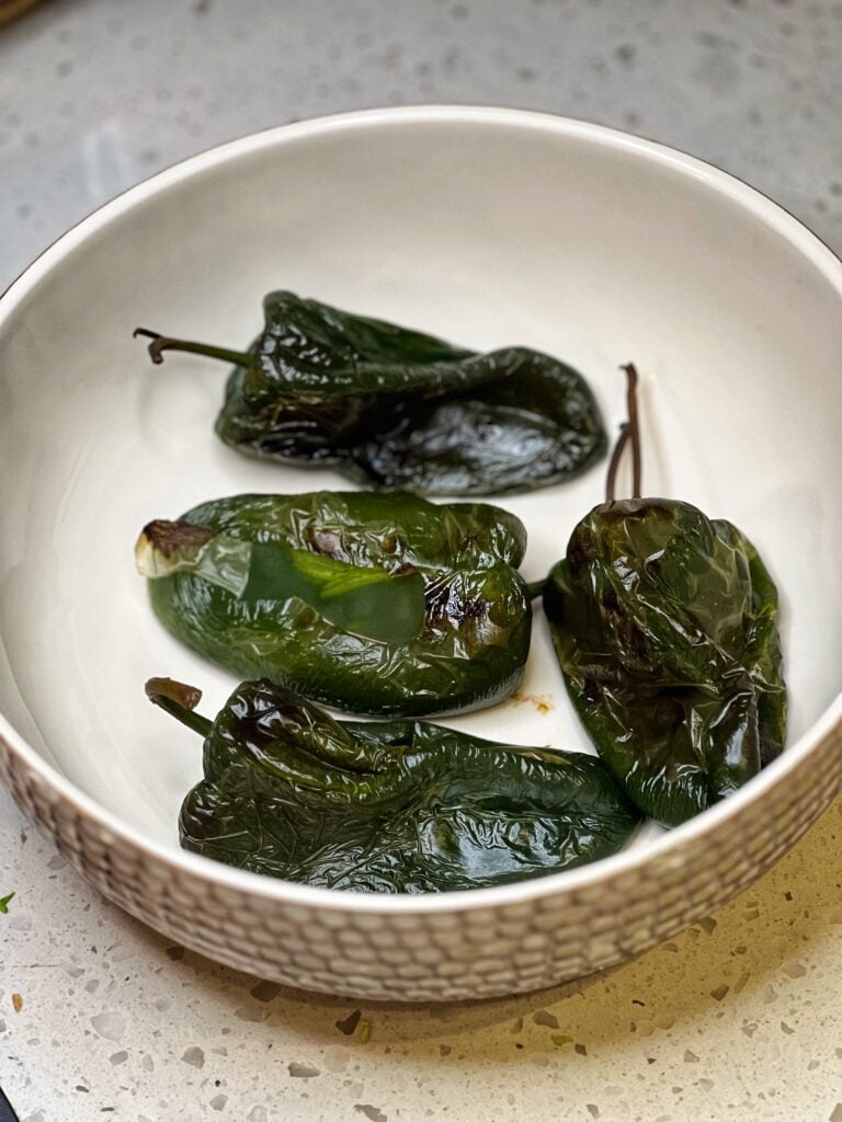Four roasted poblano peppers sitting in a bowl.