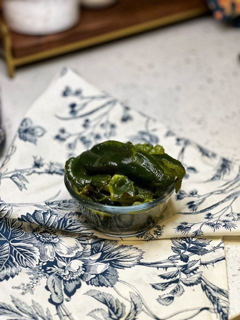 Roasted poblano peppers with skin, stem and seeds removed sitting in a small glass bowl.