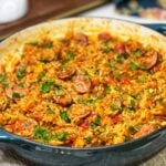 A pan of Andouille Chicken Jambalaya. The rice is red in color from tomatoes and the dish is garnished with fresh chopped parsley.