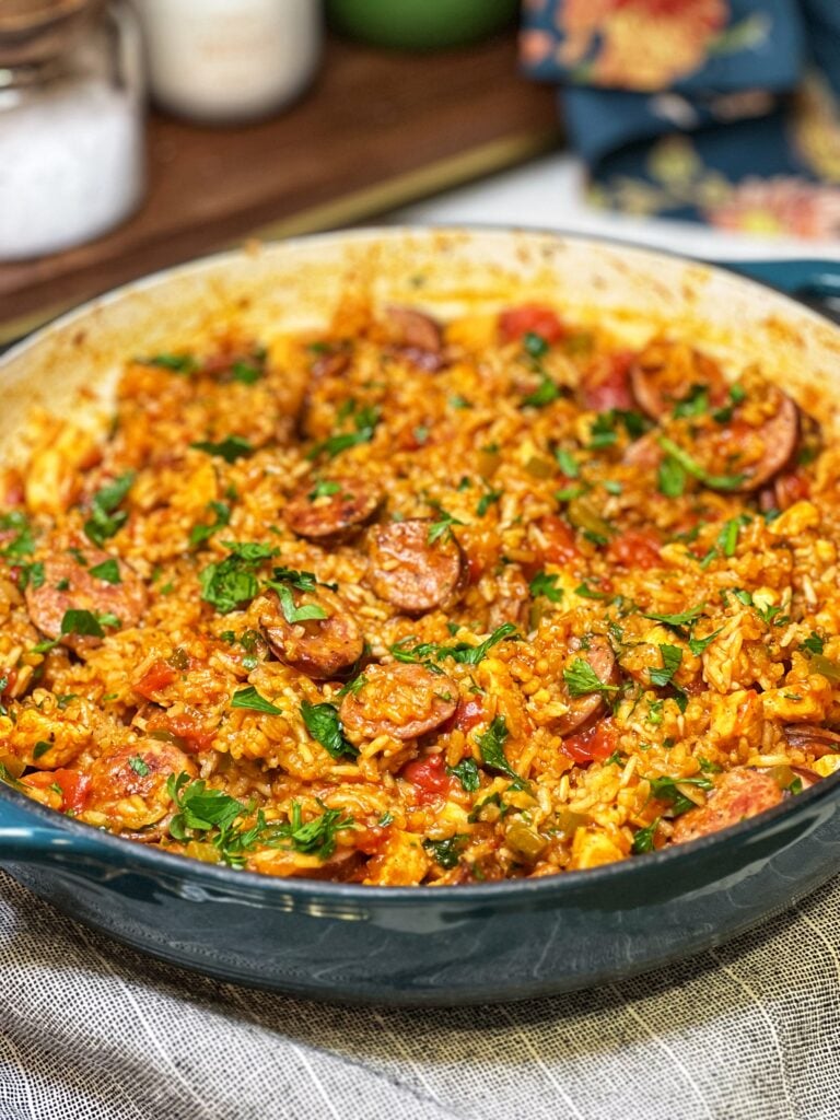 A pan of Andouille Chicken Jambalaya. The rice is red in color from tomatoes and the dish is garnished with fresh chopped parsley.