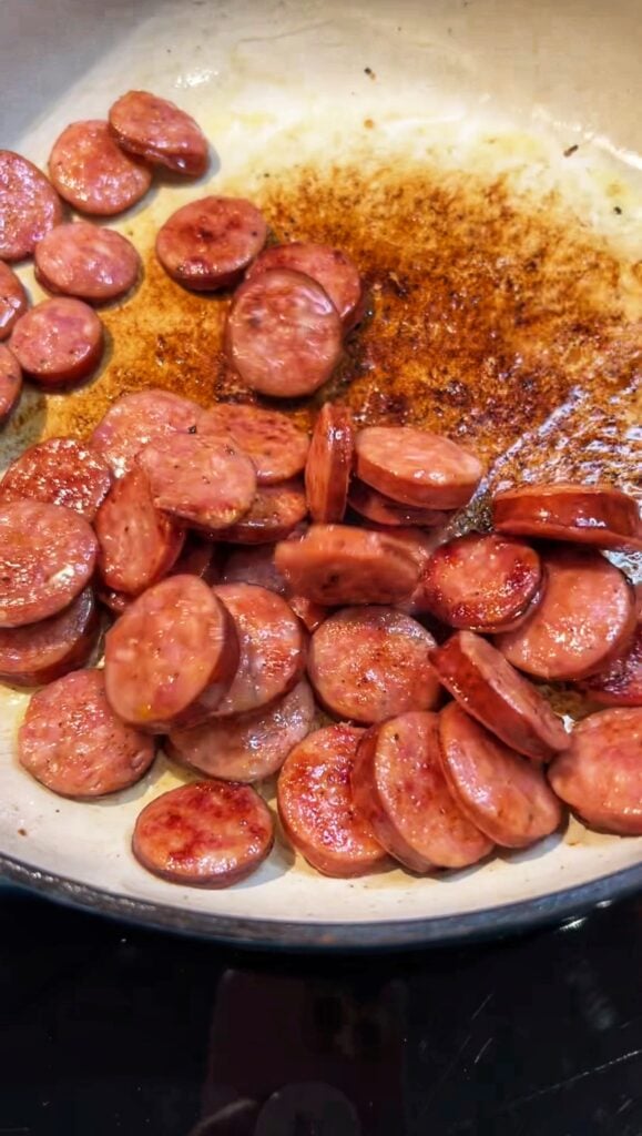 Rounds of andouille sausage browned in a pan.