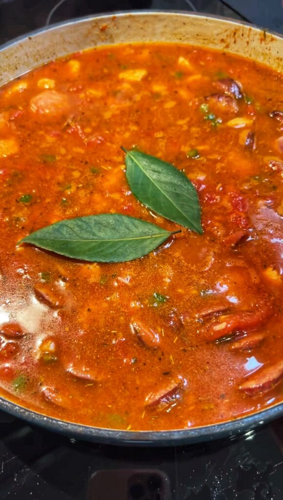 Chicken stock in a pan of rice, tomatoes and sautéed vegetables. Two bay leaves are floating on top.