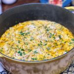 A pot of creamy chicken noodle soup. The soup has a yellowish hue and is garnished with fresh parsley.