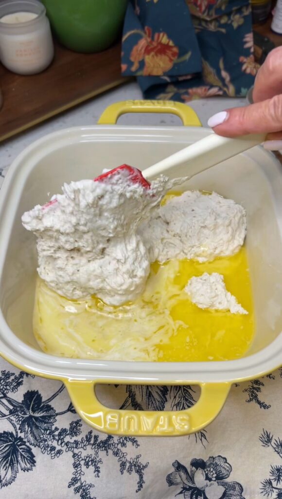 Melted butter in a casserole dish being topped with biscuit dough.