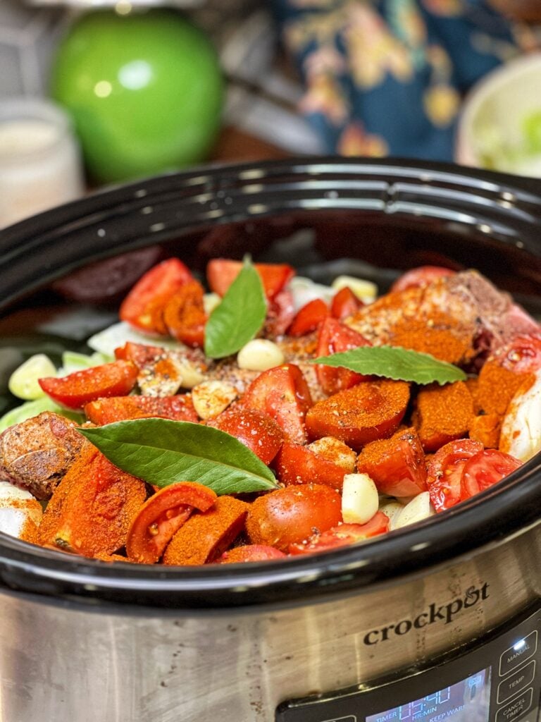 Chopped tomatoes, bay leaves, seasonings, cabbage and pork ribs in a slow cooker.
