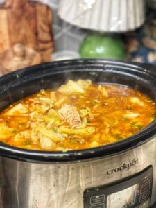 A crockpot of pork and cabbage stew. The stew is light red in color.