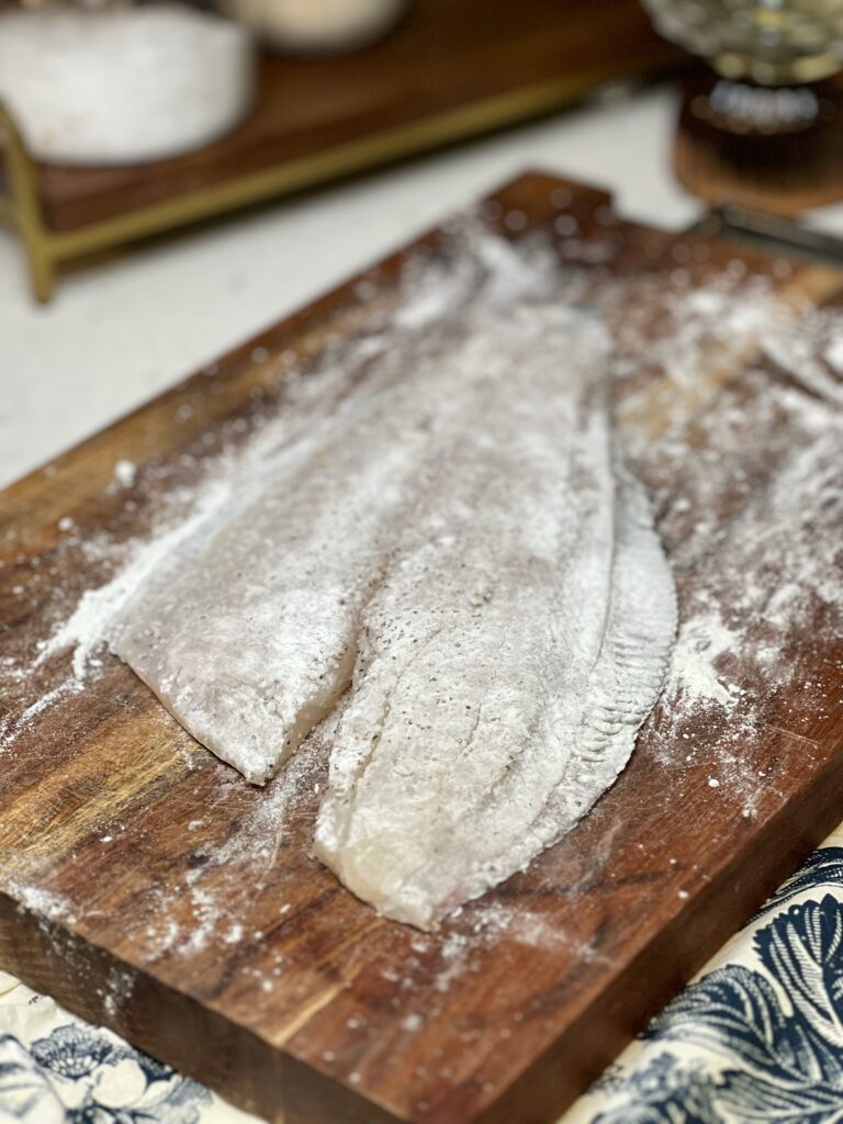 A flour-dredged flounder filet sitting on a wooden cutting board.