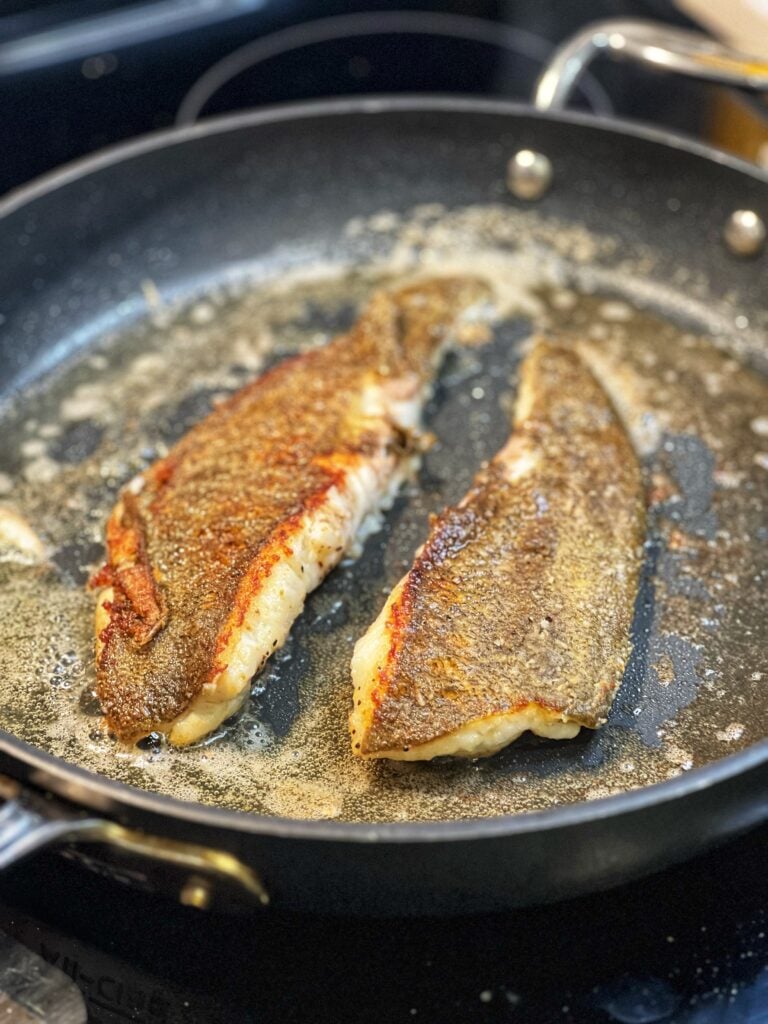 Two flounder filets searing in a cast iron pan.
