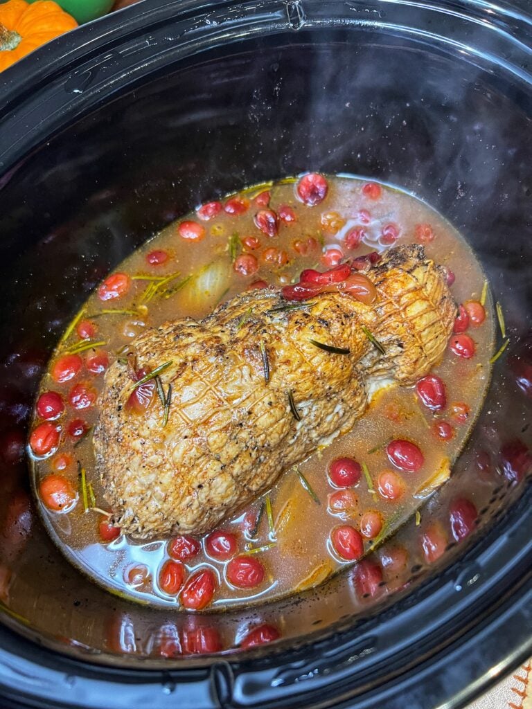 A cooked boneless turkey roast in a crockpot with the liquid and cranberries.