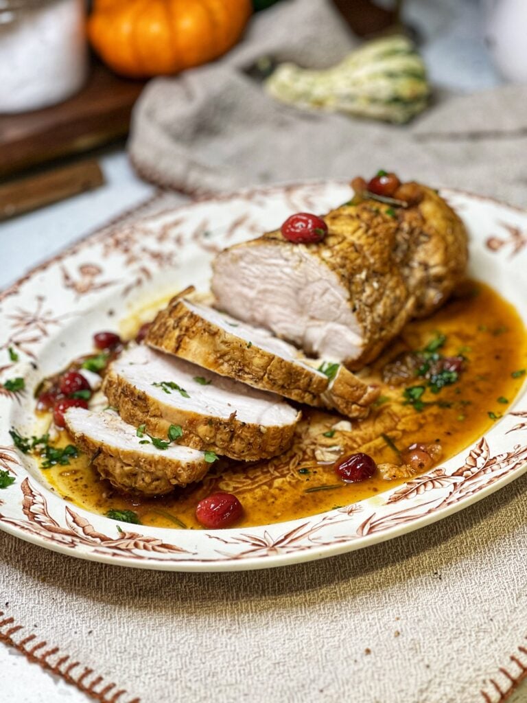 A crockpot boneless turkey roast sliced on a platter with the juices and cooked cranberries.