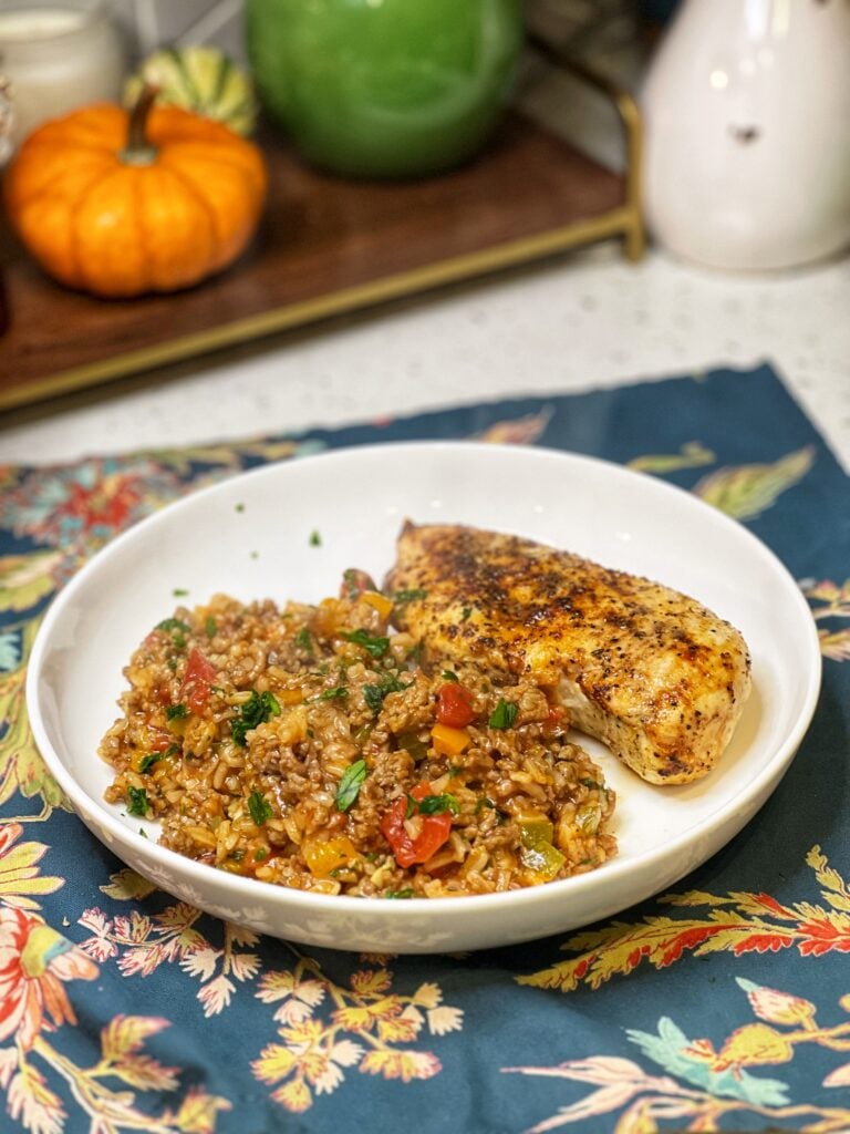 Ground beef and rice with a seared chicken breast in a white bowl.