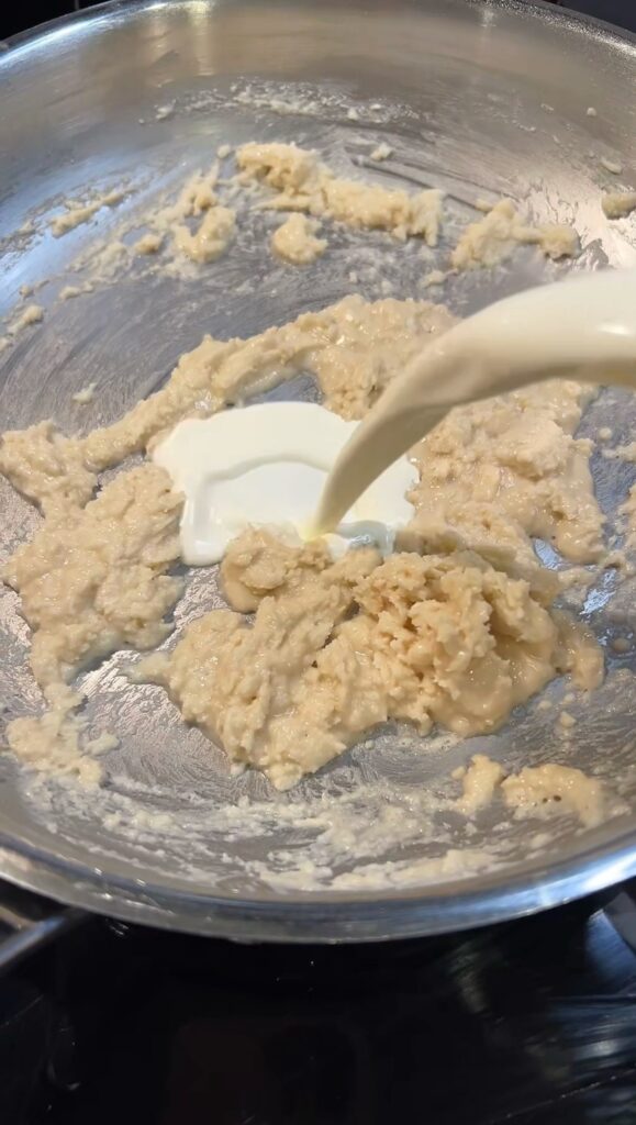 Pouring heavy cream into a pan with a roux mixture.