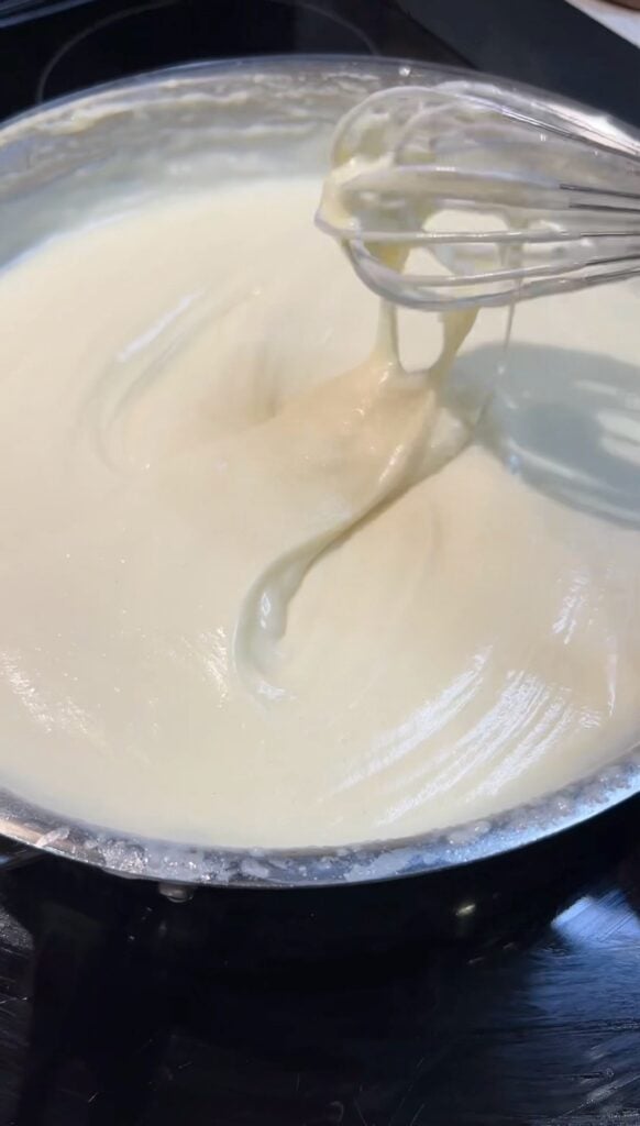 A mornay sauce in a pan. The sauce is smooth and creamy shown with a whisk.