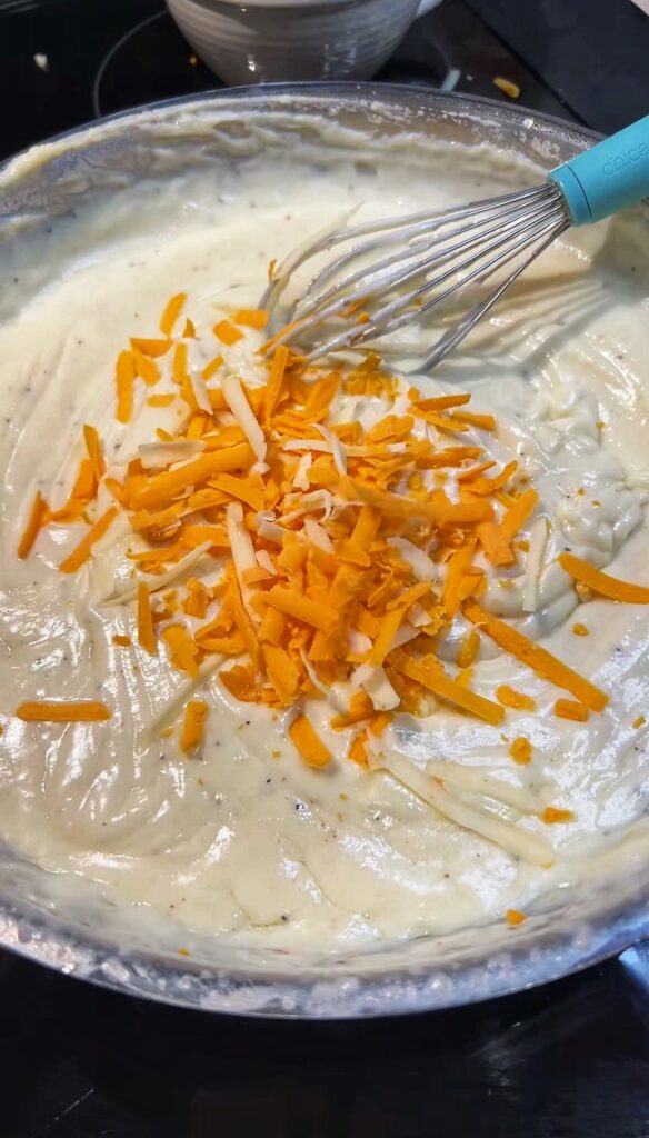 Shredded white and yellow cheddar cheese being whisked into a creamy white sauce for Cauliflower au Gratin.