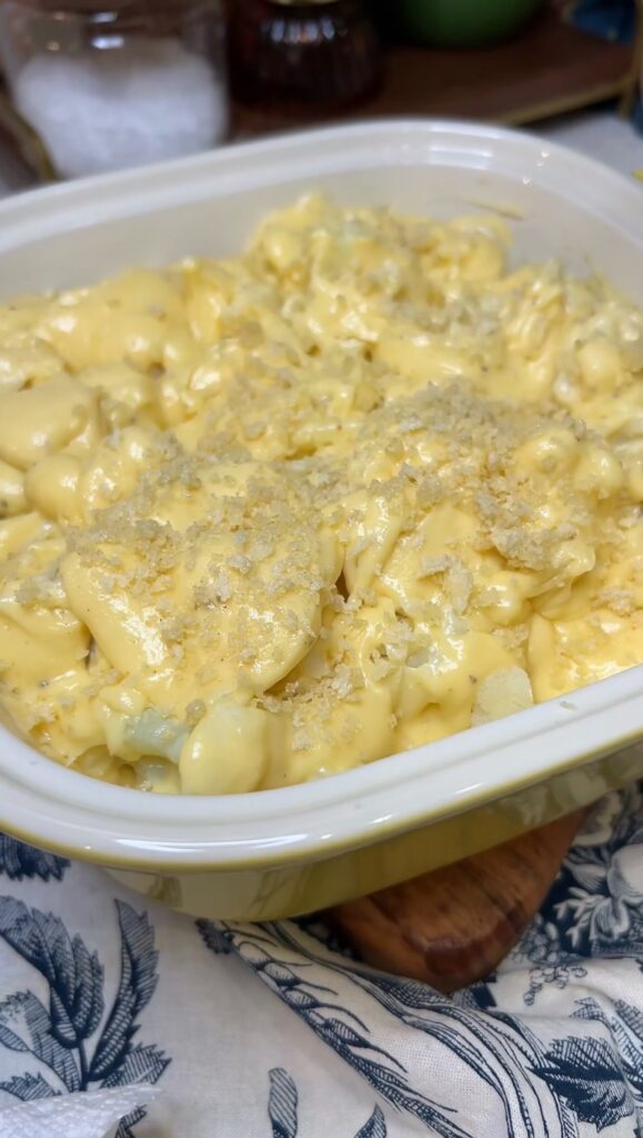 Cauliflower with cheese sauce topped with buttery panko in a yellow baking dish ready to bake.