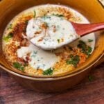 A brown bowl of she crab soup that is garnished with fresh parsley and paprika. The image is showing a wooden spoonful of the soup over the bowl.