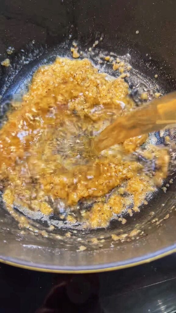 Pouring seafood stock into a pot with sautéed vegetables.