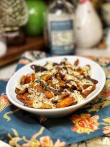 A white platter or roasted carrots with maple aioli. The sauce is white and the carrots are colorful.