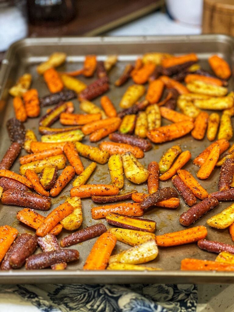 Rainbow baby carrots cut in half and seasoned laying in a single layer on a baking sheet.