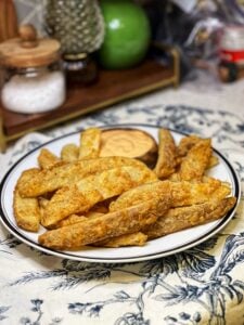 A white platter of crispy potato wedges. The wedges are fried and served with a side of chipotle mayo.