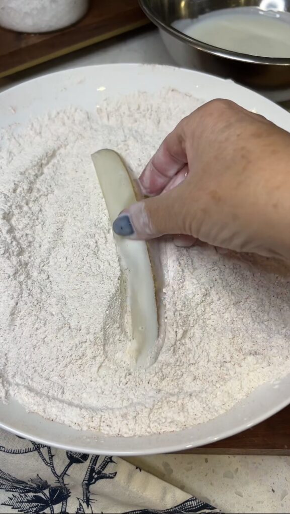 Dredging a par-boiled potato that is coated in buttermilk in a seasoned flour mixture.