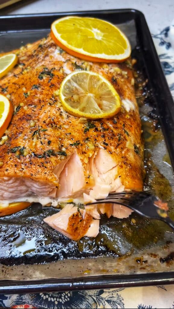 Showing the corner of a citrus herb butter salmon filet and how easily it's flaking with a fork after baking.