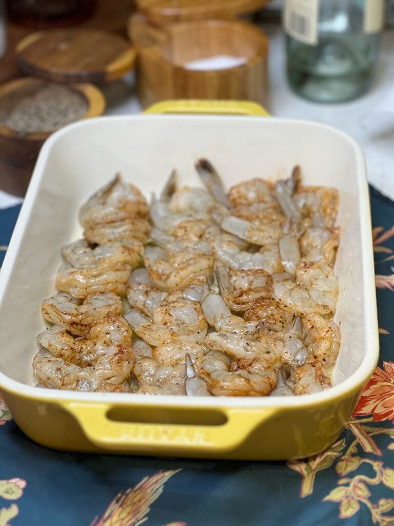 Seasoned, tail-on shrimp laying in a single layer in a yellow, rectangular casserole dish.