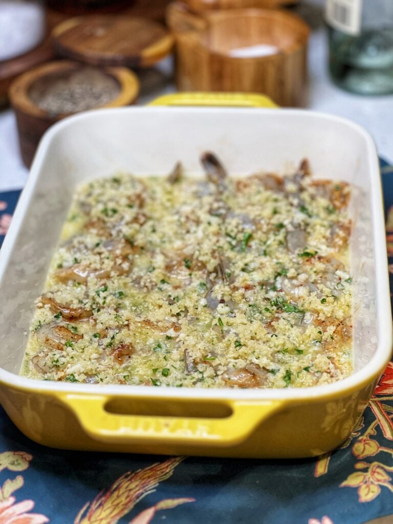 Shrimp scampi ready to bake. The shrimp are in an even layer in a casserole dish covered with a buttery mixture and topped with a panko breadcrumb mixture.