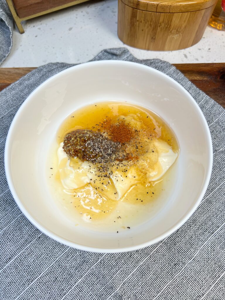 Ingredients in a white bowl for Honey Mustard Dipping Sauce. The ingredients include mayo, mustard, honey, and paprika.