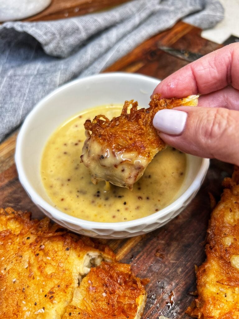 Me dipping a piece of fried chicken in a small white bowl of honey mustard dipping sauce. The sauce has a yellowish hue with flecks of grainy mustard.