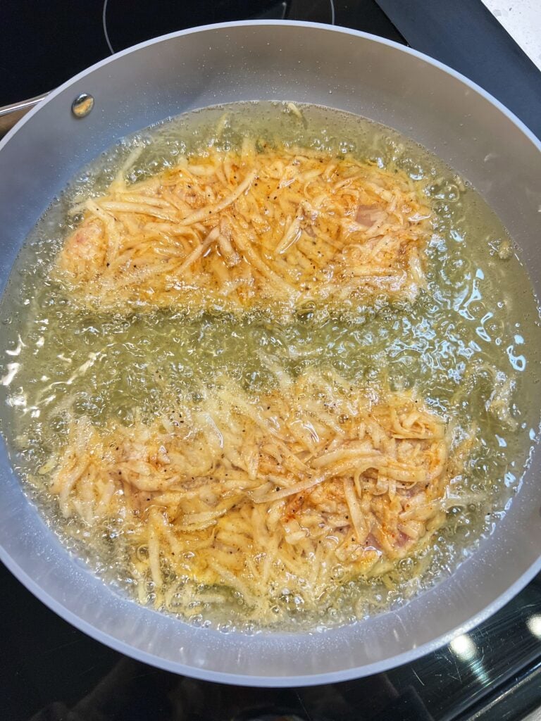 Two potato crusted chicken breasts frying in a pan of oil.