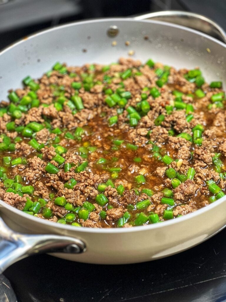 A pan of ground beef and green bean stir fry. The green beans are diced and both are in a brown sauce.