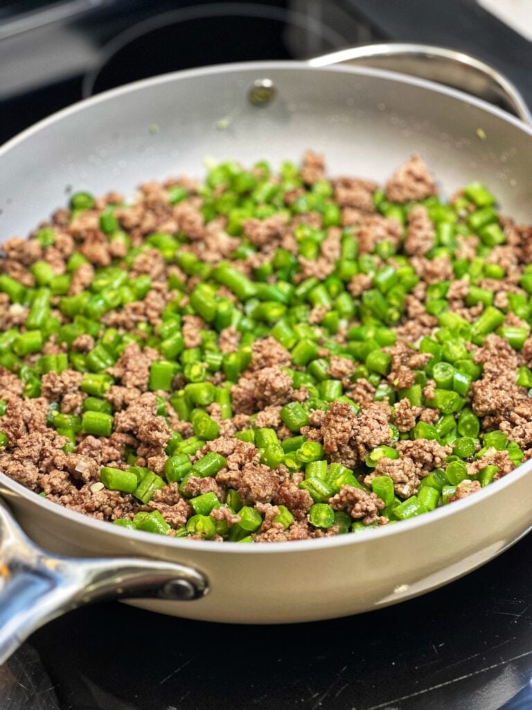 Diced green beans and ground beef in a pan.