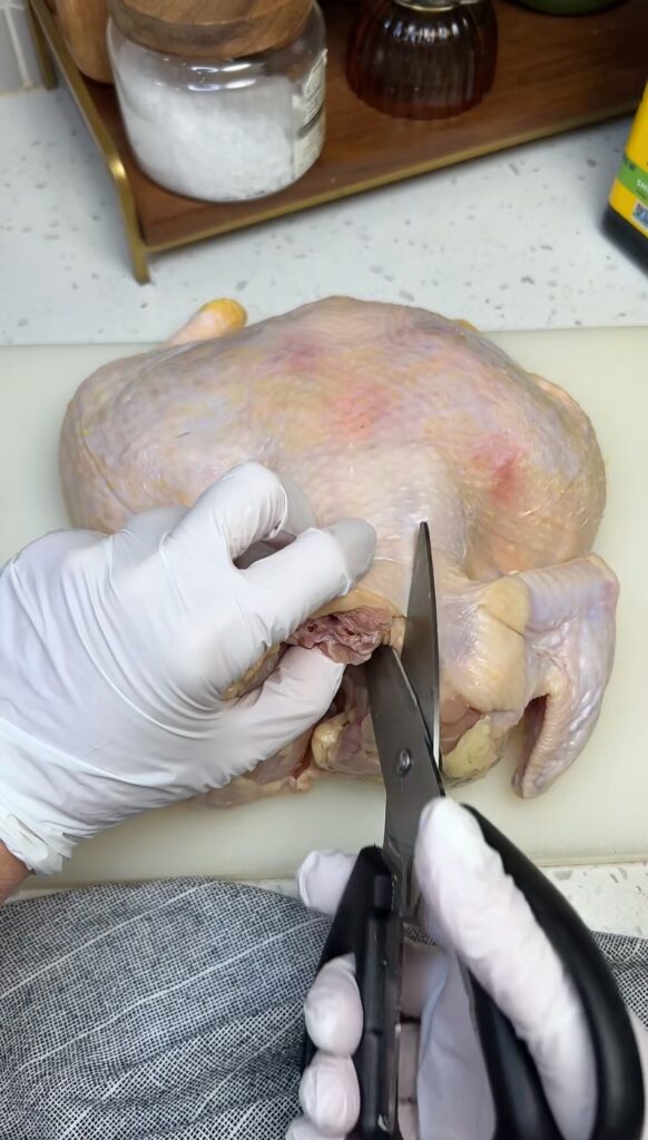 A whole chicken laying on a white plastic cutting board. I am getting ready to use kitchen shears to cut out the backbone. I am doing this to show how to spatchcock a chicken.