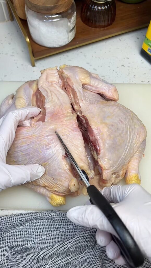 Cutting through the left side of a whole chicken's backbone for spatchcocking. The right side is already cut through.