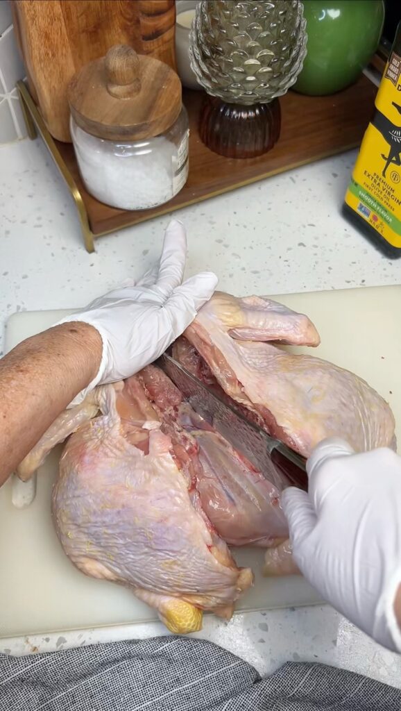Using a knife to break the breast bone of a whole chicken to show how to spatchcock a chicken.