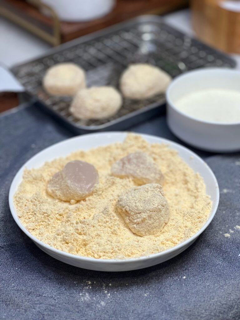 Three scallops sitting in a bowl of seafood seasoning flour.
