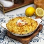 Baked Dungeness crab imperial in a small casserole dish that is browned on the top and garnished with fresh parsley and small pieces of crabmeat.