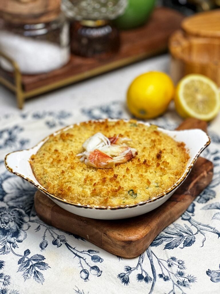 Baked Dungeness crab imperial in a small casserole dish that is browned on the top and garnished with fresh parsley and small pieces of crabmeat.