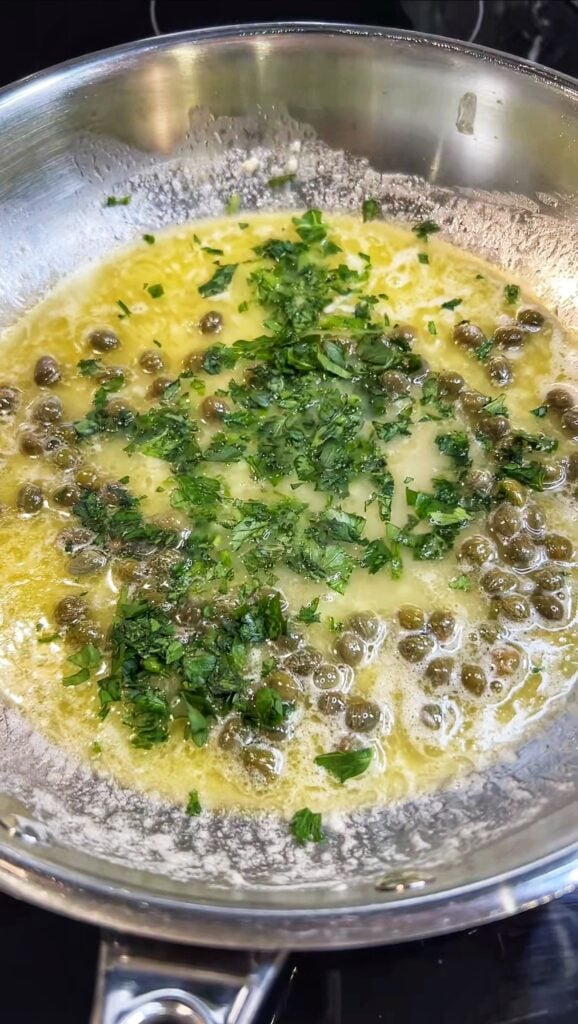 Lemon butter garlic sauce with capers and fresh chopped parsley in a stainless steel pan.