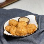 Homemade chicken nuggets that are golden brown sitting inside a small flat bowl with a small wooden bowl of honey mustard sauce.