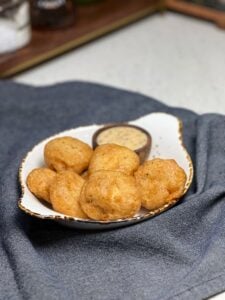 Homemade chicken nuggets that are golden brown sitting inside a small flat bowl with a small wooden bowl of honey mustard sauce.